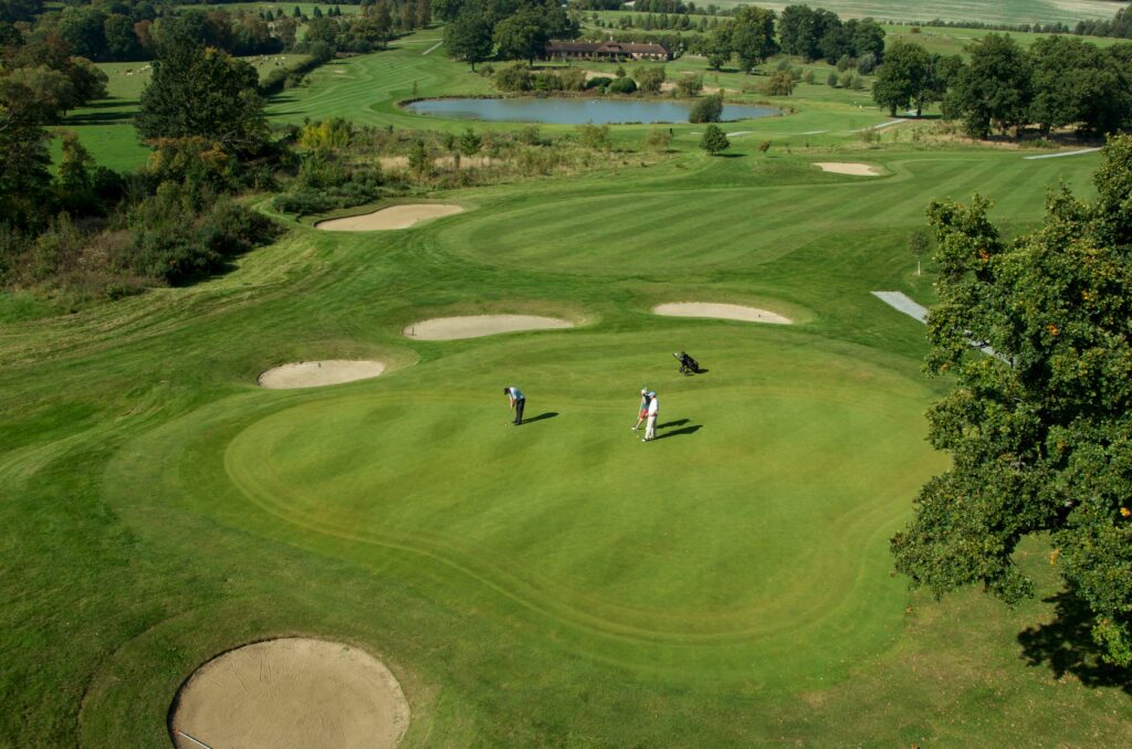 Three male golfers on a putting green from a drone perspective on a Golf course in Surrey, England, UK