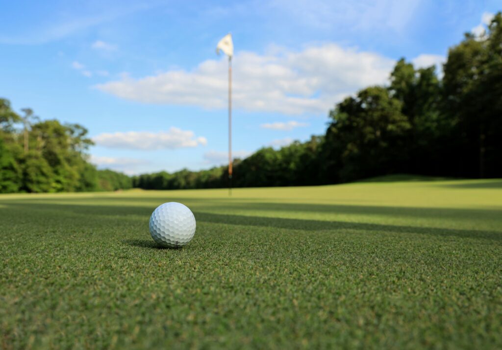 close up of golf ball on the green with course in background to represent golf club