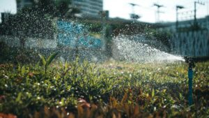 sprinklers watering grass with fence in background, representing water bills rising during summer