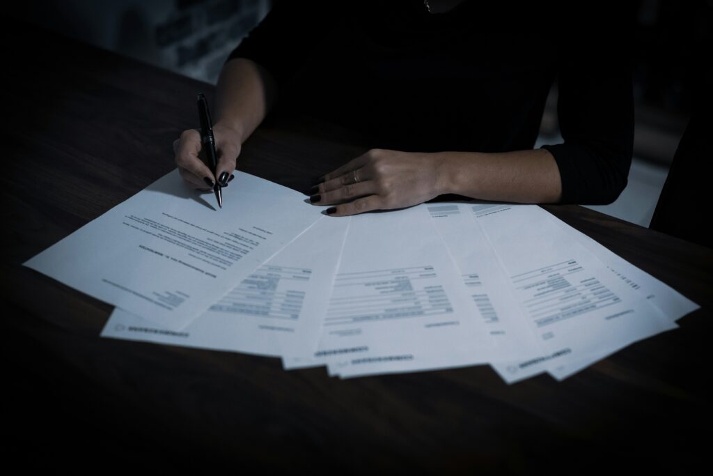 a woman sitting at a table with lots of contracts spread out in front of her, she is signing one, representing auto renewal
