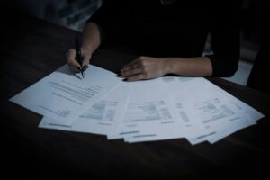 a woman sitting at a table with lots of contracts spread out in front of her, she is signing one, representing auto renewal